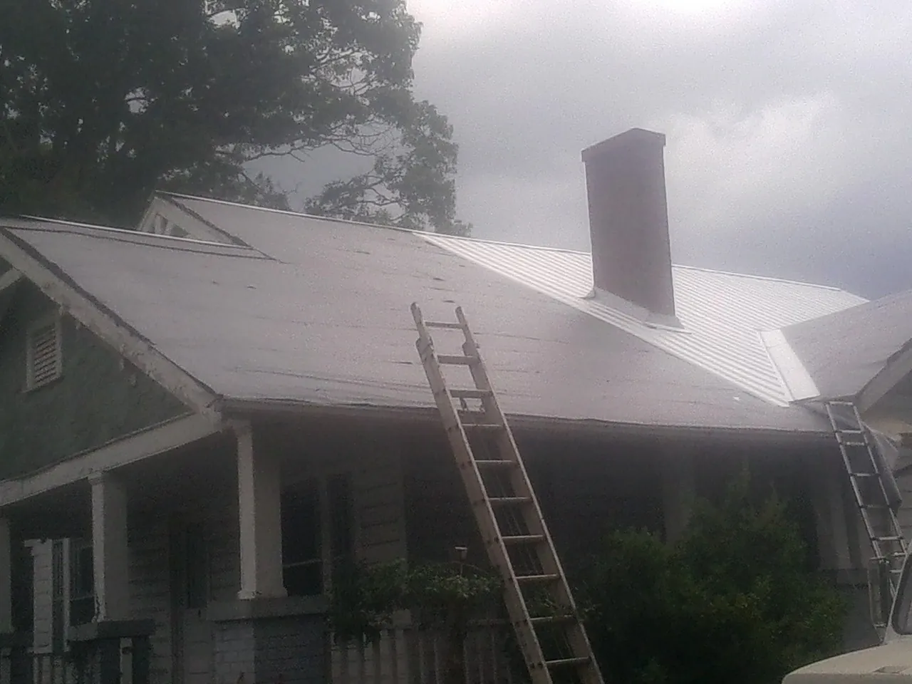 Ladders against a metal roof on an older home with a brick chimney in Hebron