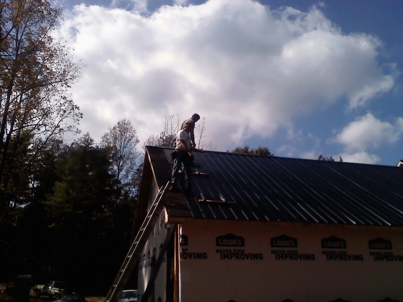 Roofer fastening dark metal panels high against a cloudy sky, from a Roof Inspection job in Hebron